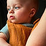 baby, child, face, blue_eyes, orange_cloth, arm, skin, person, portrait, holding, closeup, expression, indoor, soft_light, gentle, candid, human, infant, looking_away, parent