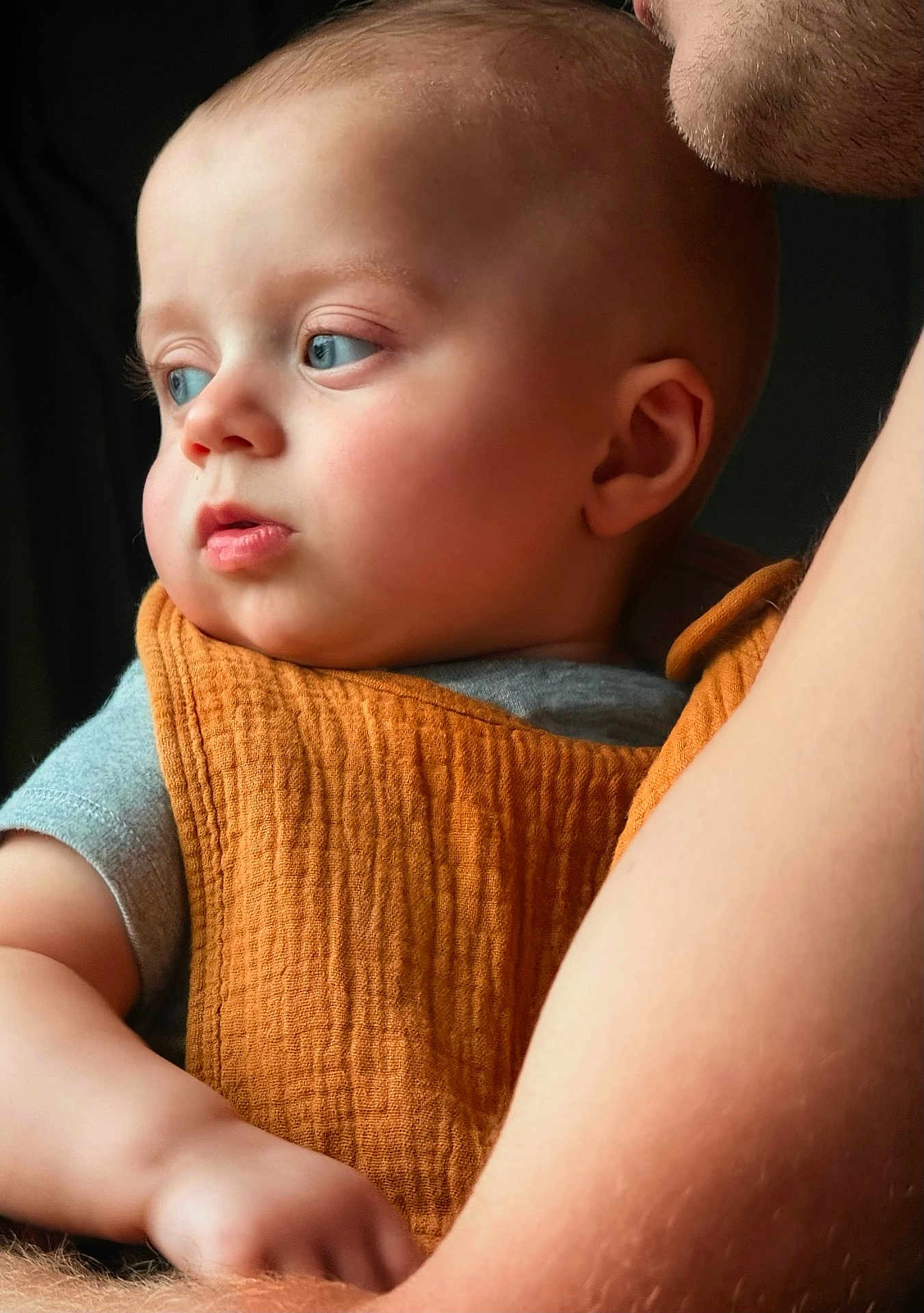 Messer joined the competition — help win amazing prizes! baby, child, face, blue_eyes, orange_cloth, arm, skin, person, portrait, holding, closeup, expression, indoor, soft_light, gentle, candid, human, infant, looking_away, parent