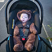 Oliver is registered to the contest to win money with this photo: baby, stroller, infant, child, outdoor, cute, fur_suit, black, seatbelt, car_seat, walkway, sidewalk, urban, expression, wide_eyes, bundle_up, winter_clothing, parked_car, road, hood