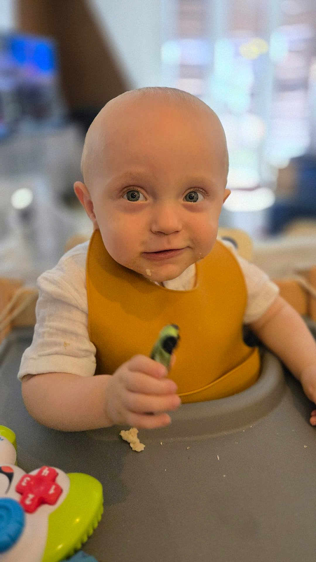 Briec participe au concours pour gagner de l'argent avec cette photo : baby, child, high_chair, bib, indoor, toy, food, hand, face, expression, curious, blurry_background, infant, cute, sitting, table, feeding, young, person, playful