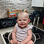 baby, child, kitchen, pot, stove, smiling, cooking_utensils, countertop, tile_wall, appliance, cute, infant, sitting, metal_pot, domestic, indoors, playful, happy, person, wearing_clothes