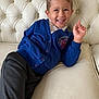 child, boy, smile, blue_cardigan, dark_pants, sofa, leather_sofa, tufted_sofa, indoor, casual, happy, portrait, young_child, person, seated, relaxed, clothing, furniture, home, comfortable