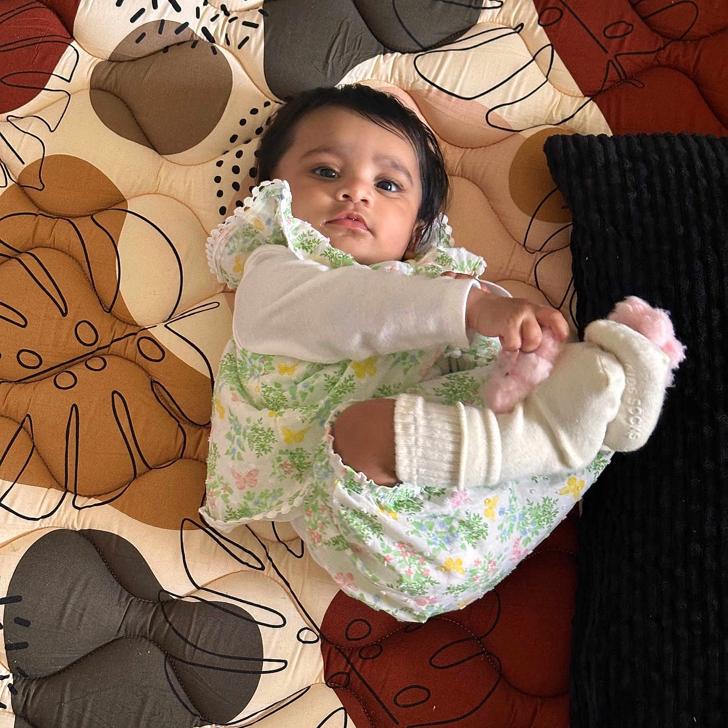 Vihaana is registered to the contest to win money with this photo: baby, blanket, child, colorful, comfort, cozy, curious, cute, floral_clothing, indoor, infant, lying_down, patterned, person, playful, portrait, quilt, socks, soft_toys, textile