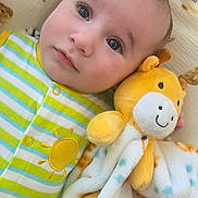 Mike is registered to the contest to win money with this photo: baby, infant, plush_toy, giraffe, blanket, teddy_bear_pattern, striped_clothing, onesie, yellow, green, blue, soft_texture, face, eyes, cute, lying_down, comfort, infant_clothing, baby_bedding, portrait