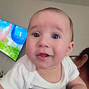 Mike joined the competition — help win amazing prizes! baby, child, face, indoor, person, curious, white_clothing, shoulder, skin, head, blue_eyes, hand, adult, television, blurred_background, expression, cute, portrait, infant, young