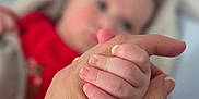 Mike is registered to the contest to win money with this photo: baby, hand, adult, holding, finger, blurred_background, red_clothing, intimacy, closeup, skin, newborn, love, bond, human, infant, touch, soft_focus, parent, child, nursery