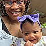 Kemani is registered to the contest to win money with this photo: woman, baby, smiling, glasses, braided_hair, headband, purple_bow, jewelry, necklace, portrait, closeup, car_interior, happy, person, child, cute, family, holding, casual_clothing, indoor