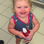 Makayla is registered to the contest to win money with this photo: toddler, child, smiling, curly_hair, blue_bows, dress, cherry_pattern, bottle, indoor, tile_floor, refrigerator, beverages, shoes, colorful, happy, person, retail, store, cute, holding