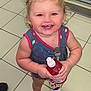 toddler, child, smiling, curly_hair, blue_bows, dress, cherry_pattern, bottle, indoor, tile_floor, refrigerator, beverages, shoes, colorful, happy, person, retail, store, cute, holding