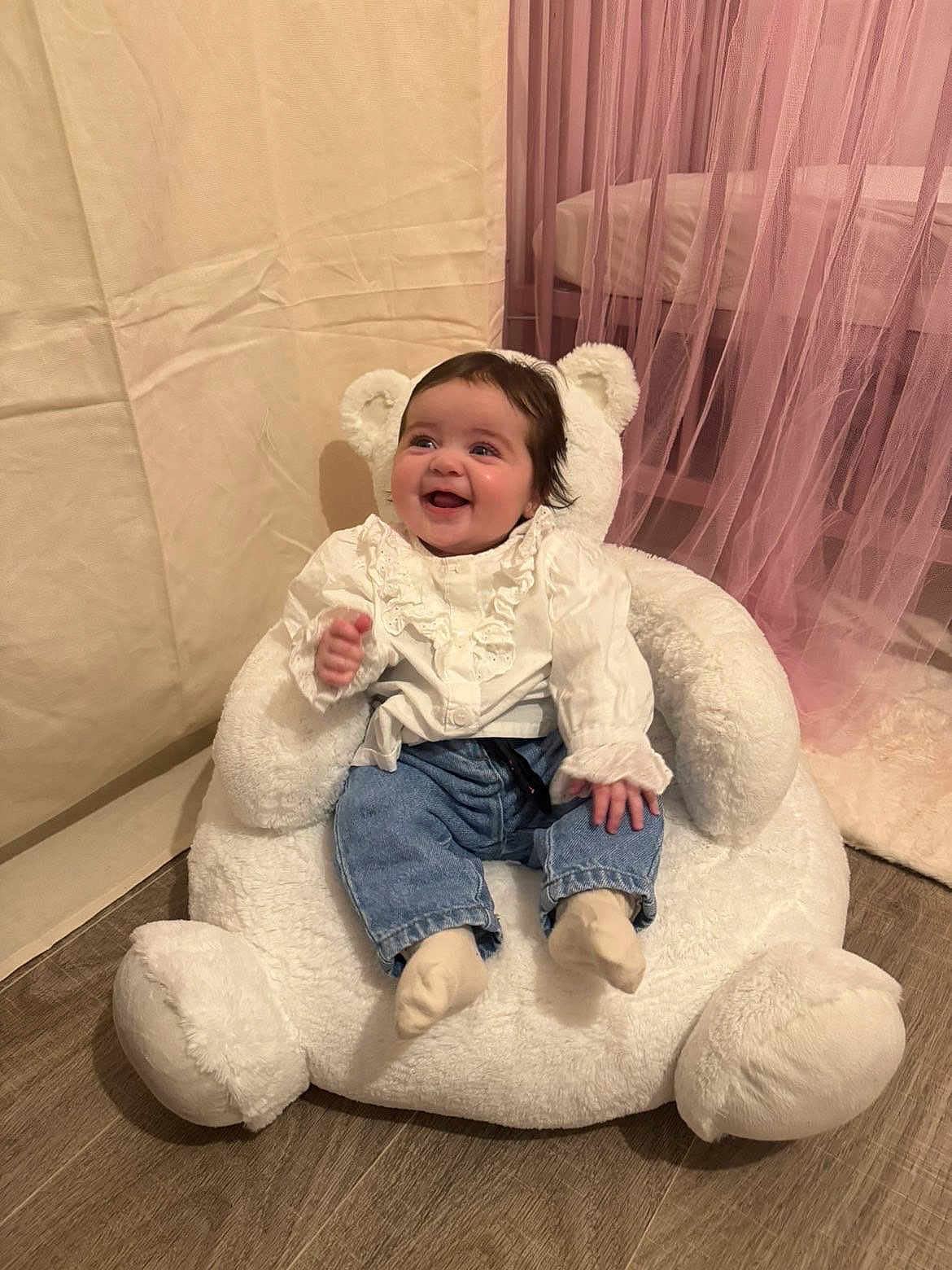 Lyana a rejoint le concours — aidez-le/la à gagner de superbes lots ! baby, child, smiling, happy, indoor, teddy_bear_chair, white_clothing, jeans, socks, soft_toys, curtains, pink, flooring, home_interior, cute, portrait, seated, infant, cozy, furniture
