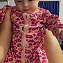 baby, infant, child, onesie, pink_clothing, leopard_print, hand, indoor, person, face, cute, young_child, sitting, portrait, soft_lighting, home, curtain, shelf, furniture, holding