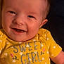 Sirena is registered to the contest to win money with this photo: baby, smiling, yellow_clothing, onesie, text_on_clothing, infant, face, happy, cute, child, portrait, closeup, skin, head, person, young_child, small_hands, heart_pattern, indoor, casual