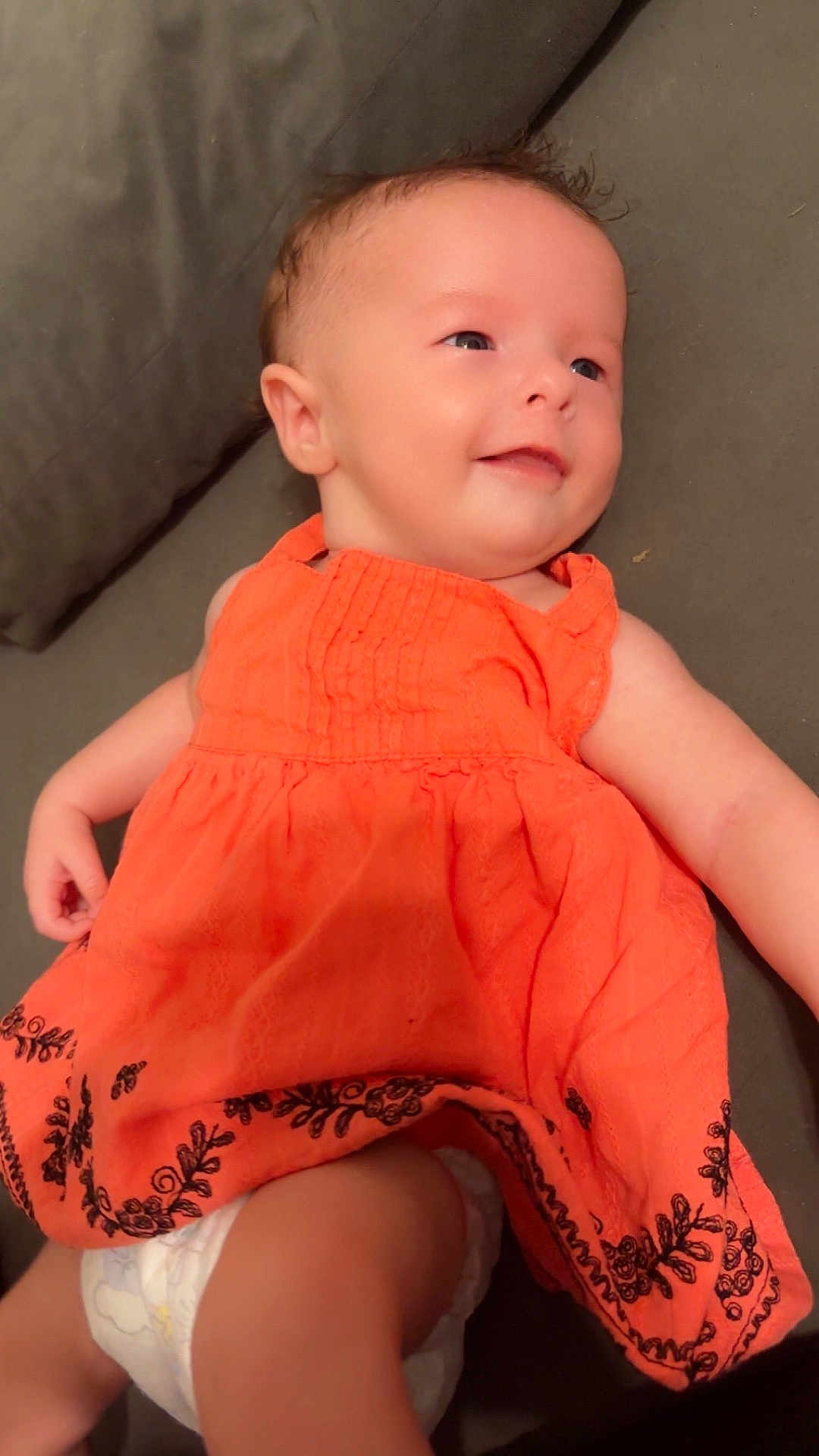 Sirena joined the competition — help win amazing prizes! baby, child, smiling, orange_dress, diaper, cushion, indoor, portrait, happy, infant, cute, young_child, face, head, skin, person, clothing, sitting, comfort, relaxation