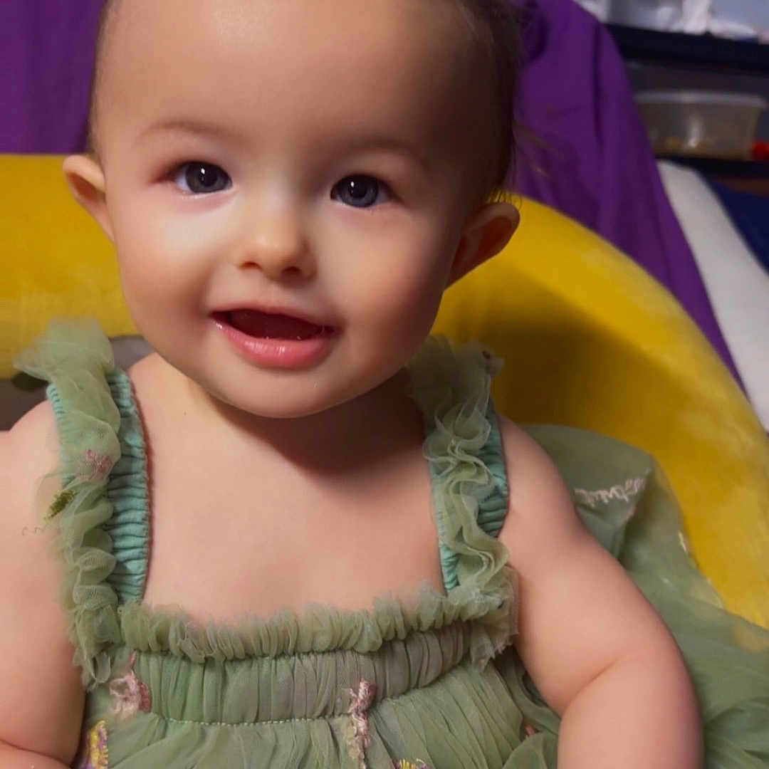 Sirena joined the competition — help win amazing prizes! baby, bottle, child, cushion, cute, ears, eyes, green_dress, hair_bow, hands, indoor, portrait, purple_blanket, smile, soft_lighting, teeth, toddler, tulle, wooden_toy, yellow_bow