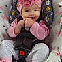 baby, child, infant, smiling, pink_headband, car_seat, safety_harness, floral_pattern, pink_socks, striped_shirt, grey_pants, cute, happy, indoors, portrait, person, seat, fabric, comfort, playful