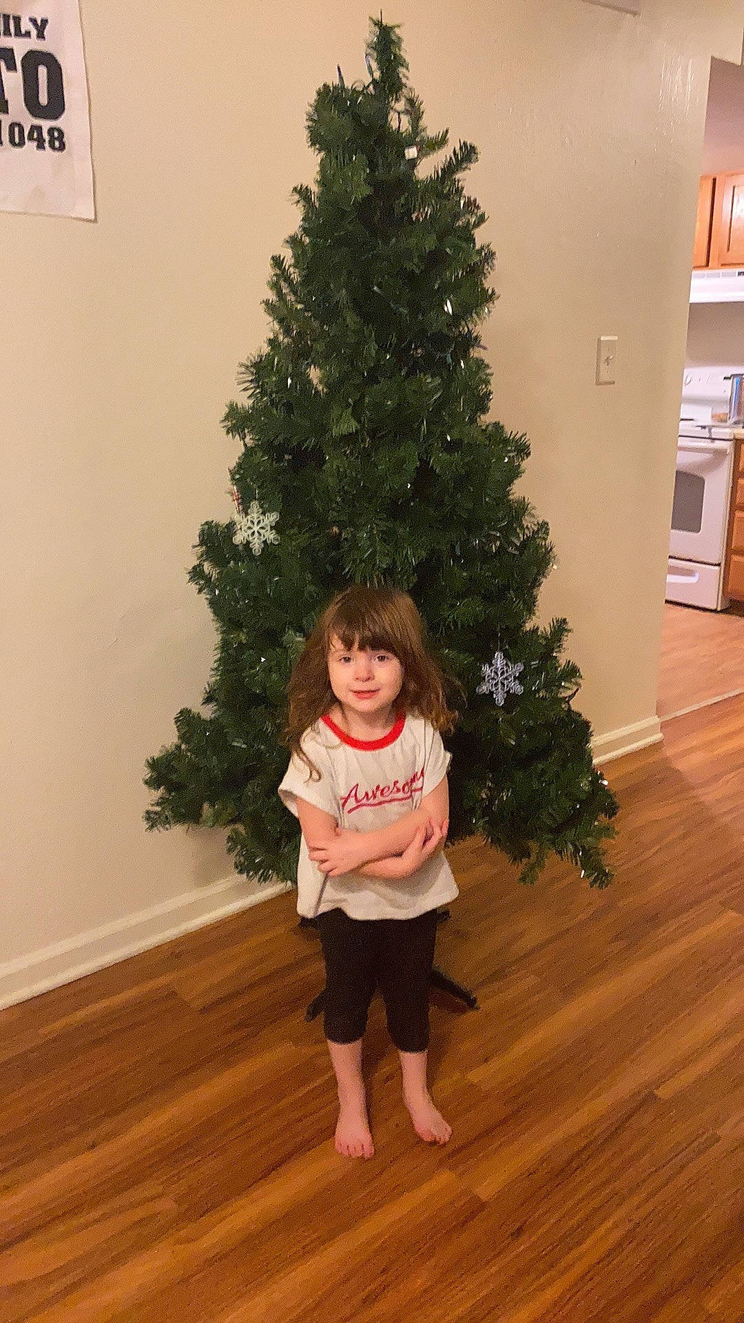 Amelia is registered to the contest to win money with this photo: christmas_decoration, christmas_ornament, christmas_tree, event, evergreen, flooring, hardwood, holiday_ornament, joy, larch, ornament, person, plank, plant, standing, toddler, tree, twig, varnish, white