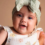 Ailany is registered to the contest to win money with this photo: baby, child, headband, bow, smiling, face, hand, floral_dress, infant, portrait, cute, happy, closeup, skin, person, soft_background, apparel, young_child, studio_photo, expression