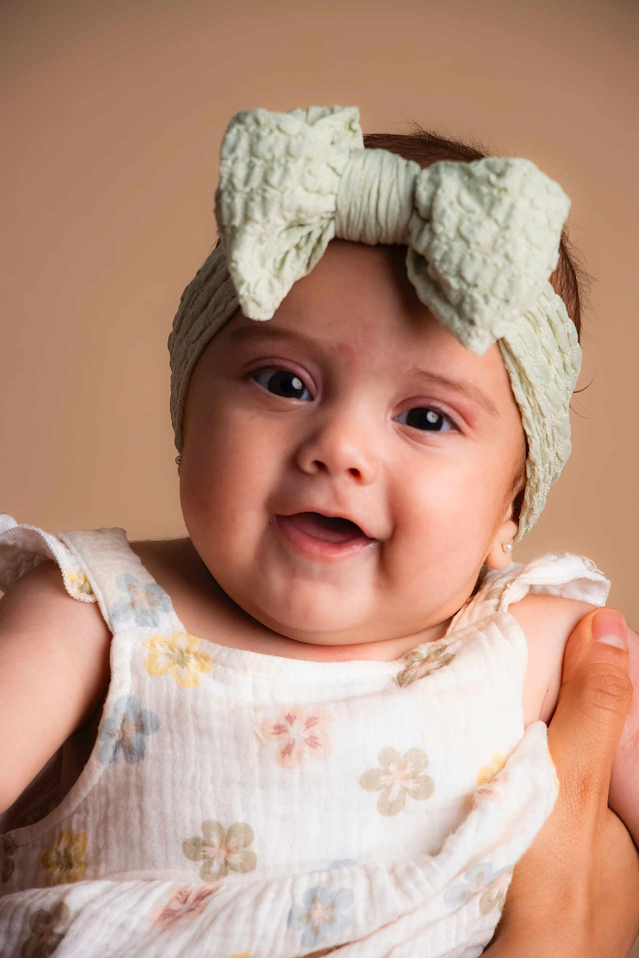 Ailany is registered to the contest to win money with this photo: baby, child, headband, bow, smiling, face, hand, floral_dress, infant, portrait, cute, happy, closeup, skin, person, soft_background, apparel, young_child, studio_photo, expression