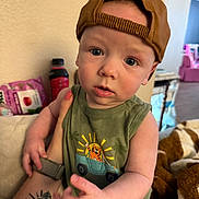 Levi joined the competition — help win amazing prizes! arm, baby, blanket, blue_eyes, cap, casual_clothing, child, curious, face, green_tank_top, hat, holding, indoor, jeep_graphic, person, portrait, soft_furniture, tattoo, tiger, toy
