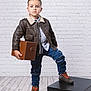 Aaron joined the competition — help win amazing prizes! child, boy, standing, pose, leather_jacket, ripped_jeans, brown_shoes, holding_box, black_box, white_brick_wall, wooden_floor, casual_clothing, fashion, portrait, indoor, foot_on_box, young, confident, short_hair, serious_expression