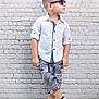 child, boy, sunglasses, white_shirt, shorts, white_shoes, brick_wall, wooden_floor, standing, pose, fashion, hair, casual, side_view, young, cool, confident, urban, portrait, smile