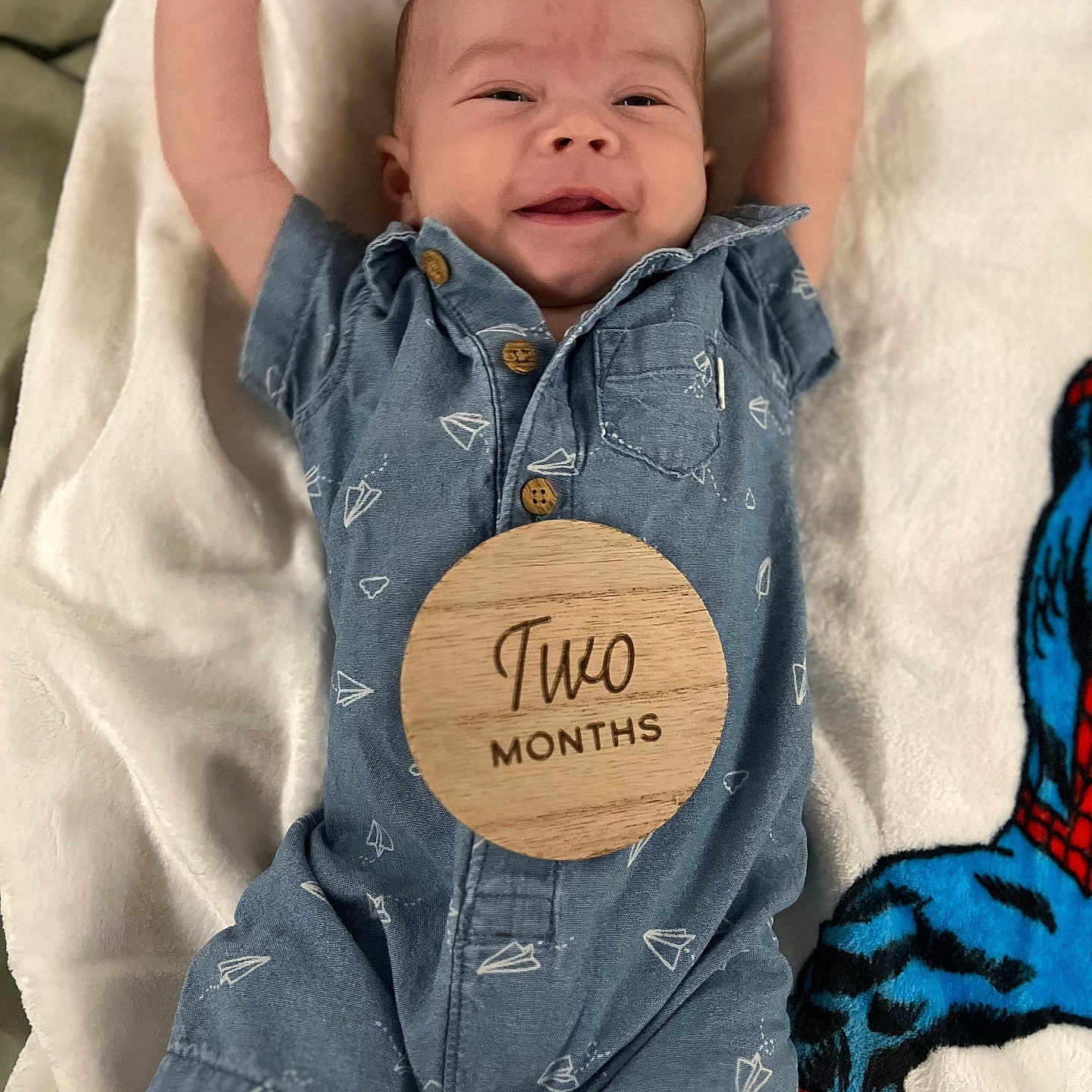 Solyn is registered to the contest to win money with this photo: arms_up, baby, baby_photo, blanket, blue_romper, child, clothing, cute, happy, indoor, infant, lying_down, newborn, paper_plane_pattern, portrait, smiling, soft_texture, spiderman_blanket, two_months, wooden_sign