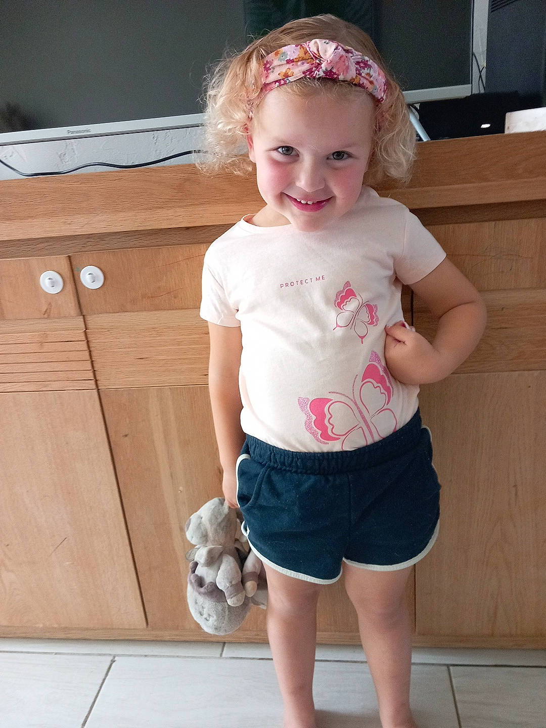 Léa participe au concours pour gagner de l'argent avec cette photo : baby_toddler_clothing, cabinetry, clothing, facial_expression, hair, hairstyle, happy, joy, leg, neck, person, pink, shorts, shoulder, sleeve, smile, standing, t_shirt, thigh, toddler