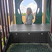 Ezekiel is registered to the contest to win money with this photo: child, playground, outdoor, play_structure, curly_hair, back_view, sky, clouds, field, grass, daylight, metal, plastic, casual_clothing, nature, solitude, relaxing, young, vacant, peaceful