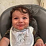 baby, child, high_chair, bib, smile, curly_hair, food, messy, face, skin, hand, clothing, elephant_graphic, reaching_hand, indoor, person, infant, cute, happy, expression