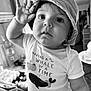 baby, child, hat, bucket_hat, shirt, text_on_clothing, indoor, portrait, black_and_white, cute, wide_eyes, hand_raised, expression, face, person, closeup, infant, home, casual_clothing, smile