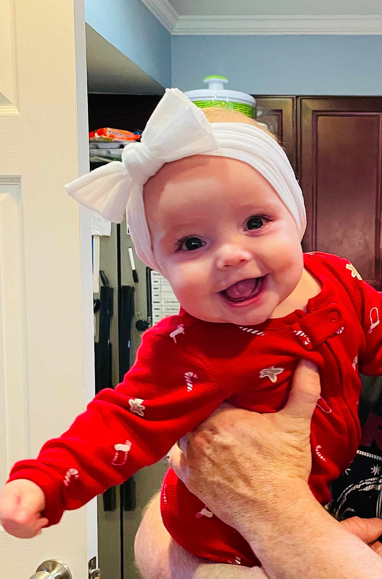 Adeline joined the competition — help win amazing prizes! baby, infant, smiling, red_clothing, white_bow, headband, hand, kitchen, cabinet, door, holiday_theme, candy_cane_pattern, gingerbread_pattern, indoor, person, happy, closeup, cute, cheerful, child