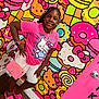 accessories, bracelet, braided_hair, child, colorful_background, donuts, fashion, girl, happy, hello_kitty, indoor, macarons, pink_clothing, portrait, purse, sandals, smiling, standing, wall_art, white_shorts