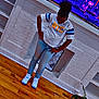 blue_stripes, bottles, casual_clothing, child, decor, floor, hair_puff, hands_on_hips, home_interior, indoor, jeans, lighting, looking_down, potted_plant, shelf, sneakers, standing, wall_art, white_tshirt, wooden_floor