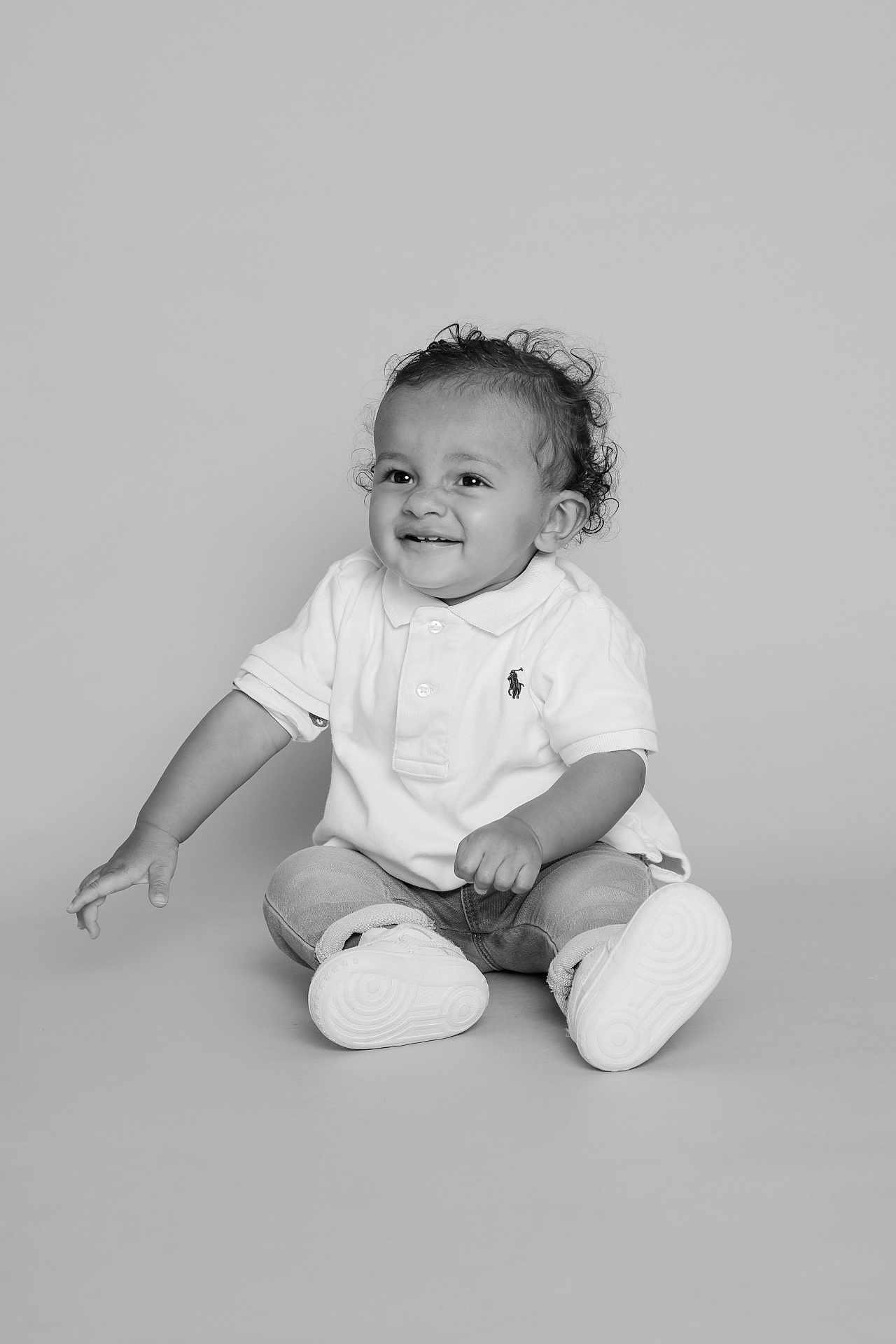 Izaac a rejoint le concours — aidez-le/la à gagner de superbes lots ! child, toddler, smiling, sitting, curly_hair, white_polo, jeans, sneakers, studio, portrait, happy, baby, cute, fashion, clothing, monochrome, black_and_white, person, young, innocent