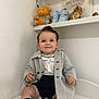 toddler, child, baby, smiling, coat, shorts, socks, indoor, white_wall, sitting, teddy_bear, baby_shoes, photo_frame, shelf, portrait, cute, happy, clothing, person, home