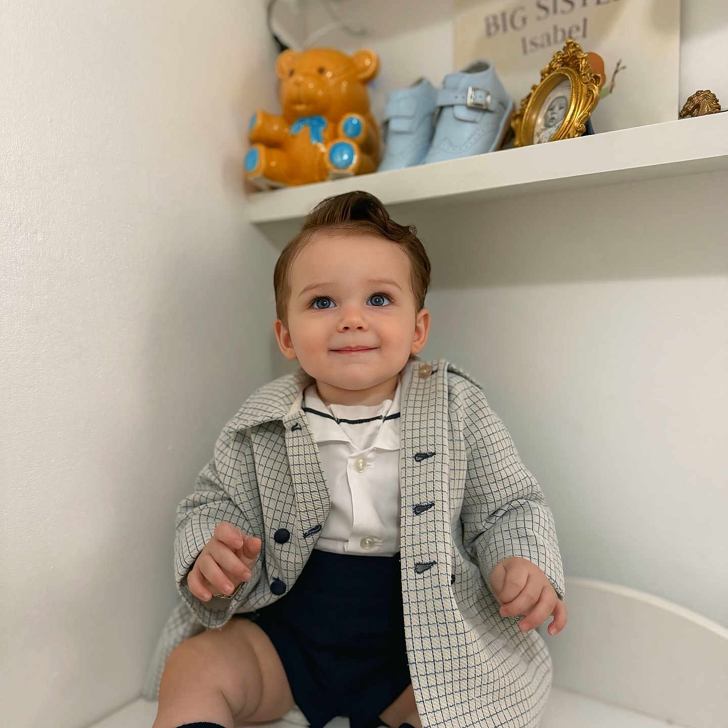 Elijah-James is registered to the contest to win money with this photo: baby, baby_shoes, child, clothing, coat, cute, happy, home, indoor, person, photo_frame, portrait, shelf, shorts, sitting, smiling, socks, teddy_bear, toddler, white_wall