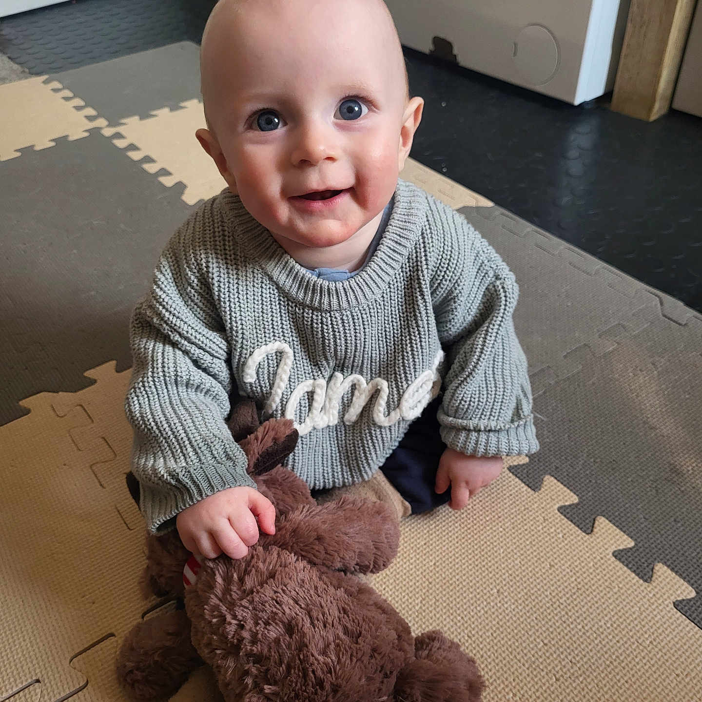 James joined the competition — help win amazing prizes! baby, baby_clothing, carpet, child, childhood, cute, floor, flooring, happy, home, indoor, knit_sweater, person, play_mat, plush_toy, portrait, seated, smiling, teddy_bear, toy