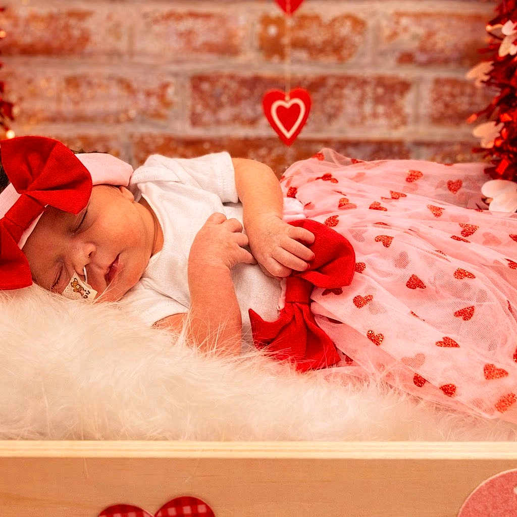 Miracle is registered to the contest to win money with this photo: baby, sleeping, infant, pink, red, bow, headband, dress, hearts, fluffy, cushion, wooden_box, decorations, brick_wall, cozy, cute, newborn, holiday, valentines, portrait