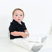 Hudson is registered to the contest to win money with this photo: toddler, child, black_polo, white_pants, gray_socks, disco_ball, sitting, indoor, white_background, curious, wide_eyes, minimalist, cute, portrait, young_child, holding_object, studio_lighting, casual_clothing, innocent, baby