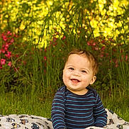 Rory is registered to the contest to win money with this photo: baby, child, smiling, grass, blanket, outdoor, nature, flowers, greenery, happy, portrait, toddler, striped_shirt, sunlight, cute, sitting, face, cheerful, playful, young