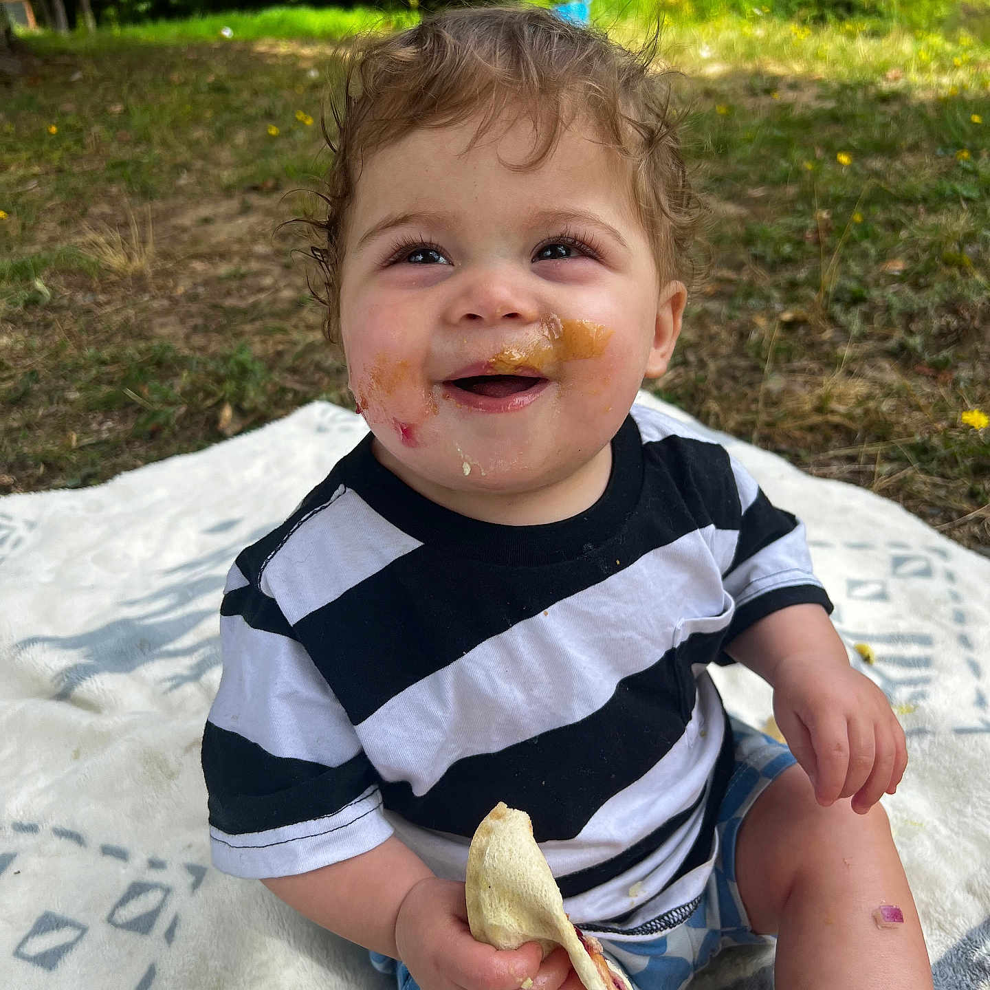 Rory joined the competition — help win amazing prizes! blanket, child, cute, daylight, face, food, grass, hands, happy, messy_face, nature, outdoor, picnic, shorts, sitting, skin, smiling, striped_shirt, toddler, young_child