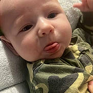 Theo is registered to the contest to win money with this photo: baby, blanket, camo, child, closeup, clothing, cozy, cute, expression, face, hand, indoor, infant, person, portrait, resting, skin, soft, tongue, young