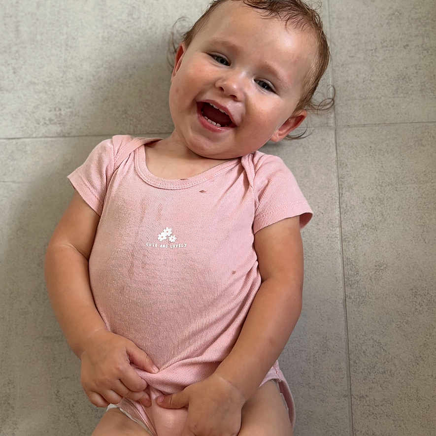 Mïa participe au concours pour gagner de l'argent avec cette photo : baby, barefoot, casual, child, cloth, cute, expression, floor, happy, indoor, lying_down, person, pink_onesie, playful, skin, smiling, tile, toddler, toy, young_child