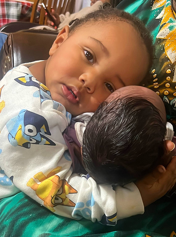 Monroe is registered to the contest to win money with this photo: baby, black_hair, cheek, child, event, forehead, fun, happy, leisure, linens, mouth, nose, person, play, room, sitting, skin, smile, tartan, toddler