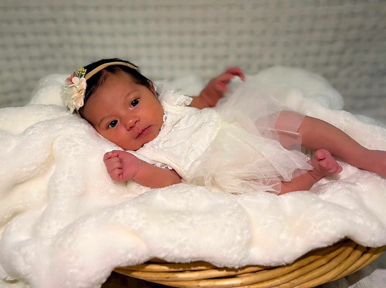 Willow is registered to the contest to win money with this photo: baby, infant, white_dress, flower_headband, blanket, basket, cute, newborn, portrait, soft_texture, lying_down, face, skin, hand, foot, cozy, indoors, child, toddler, adorable