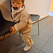 Axel participe au concours pour gagner de l'argent avec cette photo : toddler, child, pacifier, chair, indoor, tile_floor, beige_clothing, jacket, curious, standing, black_chair, floor, person, young_child, casual_clothing, baby, head, face, looking, warm_clothing