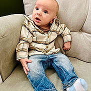 Randy is registered to the contest to win money with this photo: armchair, baby, blue_jeans, casual_clothing, child, curious, cute, expression, face, furniture, head, indoor, infant, legs, person, plaid_shirt, seated, small_hands, socks, surprised