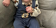 Randy is registered to the contest to win money with this photo: apparel, baby, child, clothing, comfort, couch, cute, fabric, face, foot, furniture, hand, happy, indoors, infant, mickey_mouse, overalls, person, sitting, smile