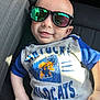 baby, child, sunglasses, smile, shirt, blue, white, car_seat, reflection, sunlight, casual, portrait, young_child, clothing, seat, cute, relaxed, person, indoor, fashion