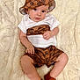 Randy is registered to the contest to win money with this photo: baby, infant, child, hat, brown_clothing, white_shirt, shorts, shoes, blanket, soft_texture, indoor, portrait, cute, sitting, small_hands, legs, feet, fashion, patterned_fabric, looking_at_camera